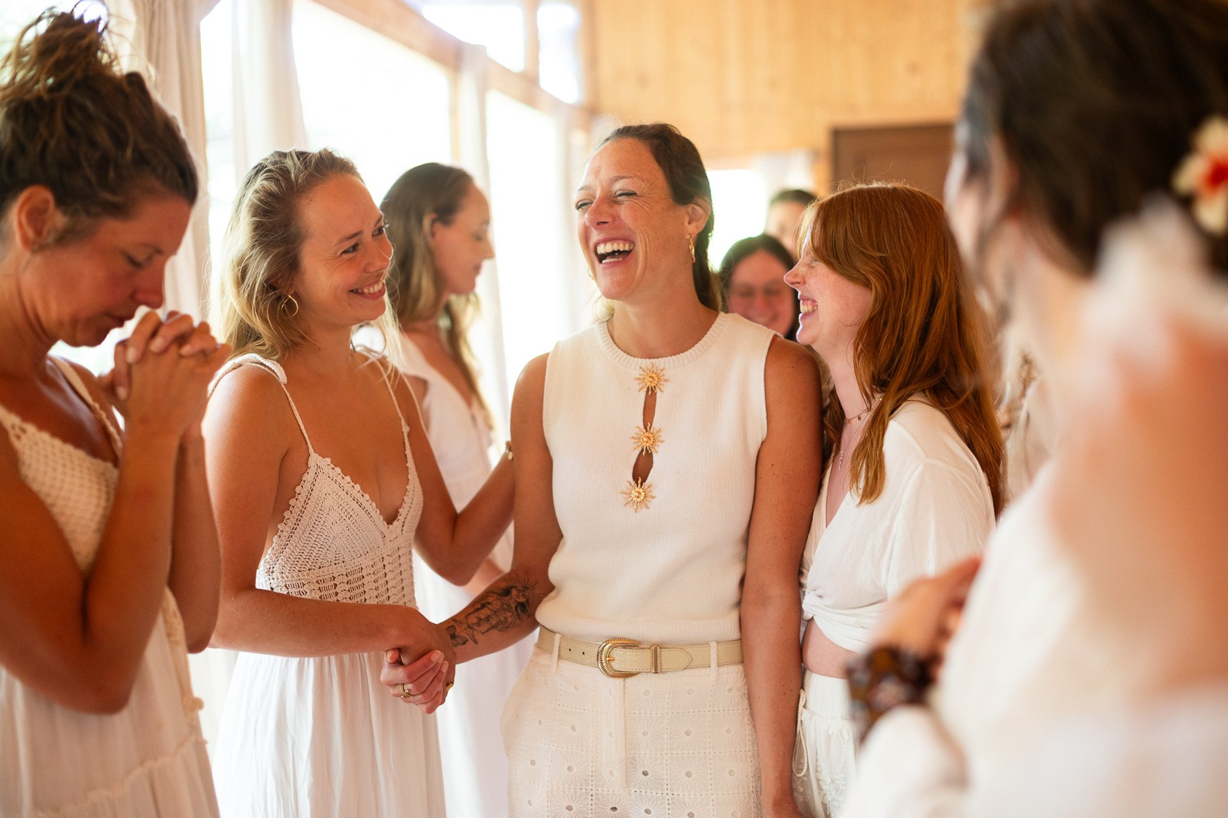 Women in white laughing together, holding hands in a circle